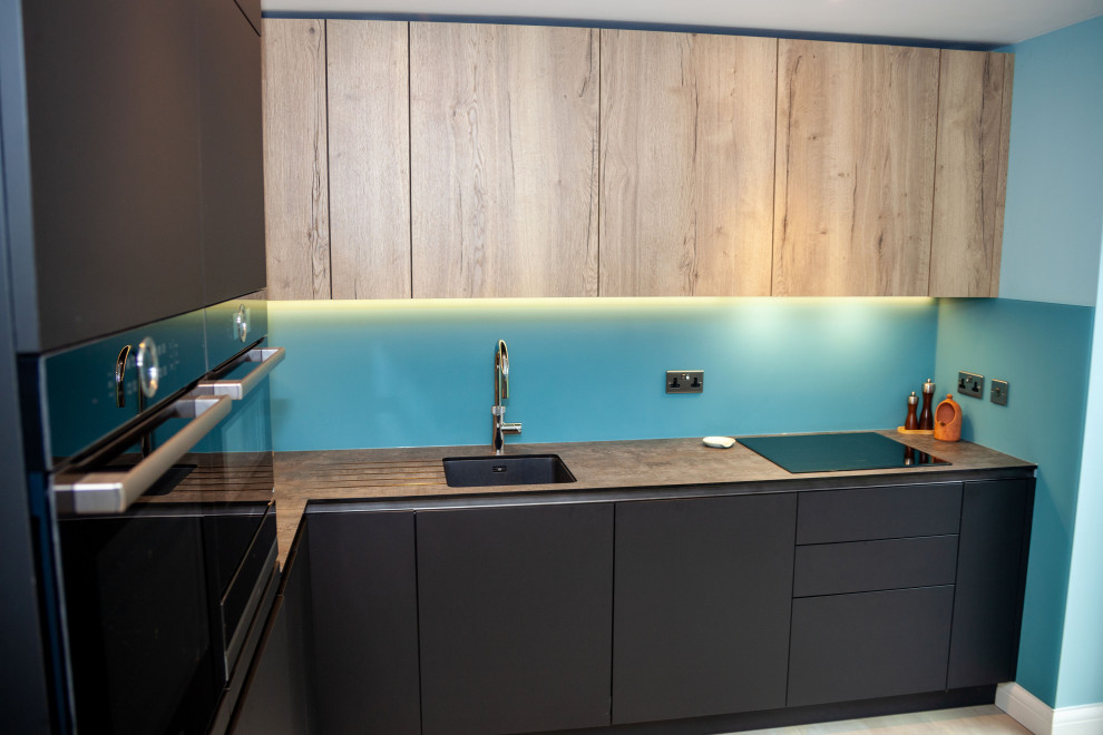 Mid-sized contemporary open plan kitchen in Other with a single-bowl sink, flat-panel cabinets, blue splashback, glass sheet splashback and black appliances.