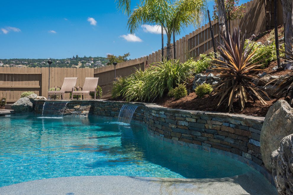 Mid-sized tropical backyard kidney-shaped pool in Sacramento with a water feature and natural stone pavers.