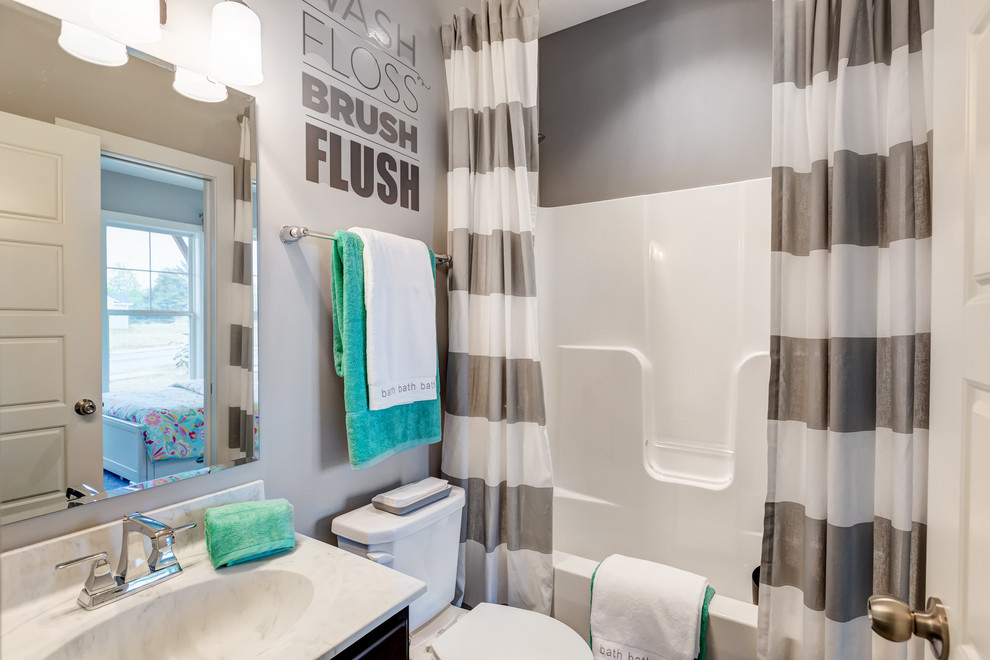 Example of a mid-sized transitional kids' tub/shower combo design with dark wood cabinets, a one-piece toilet, gray walls, an integrated sink and marble countertops