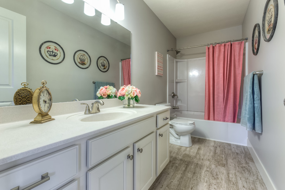 Photo of a traditional kids bathroom in Grand Rapids with an integrated sink, recessed-panel cabinets, distressed cabinets, marble benchtops, an alcove tub, a shower/bathtub combo, a two-piece toilet, grey walls and linoleum floors.