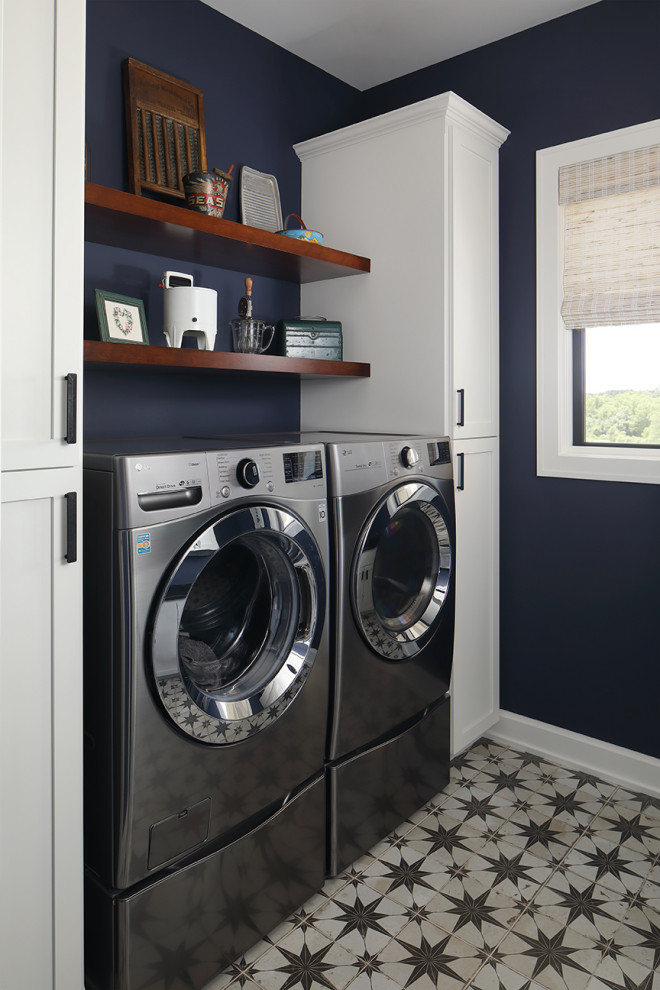 Klassisk inredning av en stor u-formad tvättstuga enbart för tvätt, med en undermonterad diskho, släta luckor, vita skåp, blå väggar, klinkergolv i porslin, en tvättmaskin och torktumlare bredvid varandra och flerfärgat golv