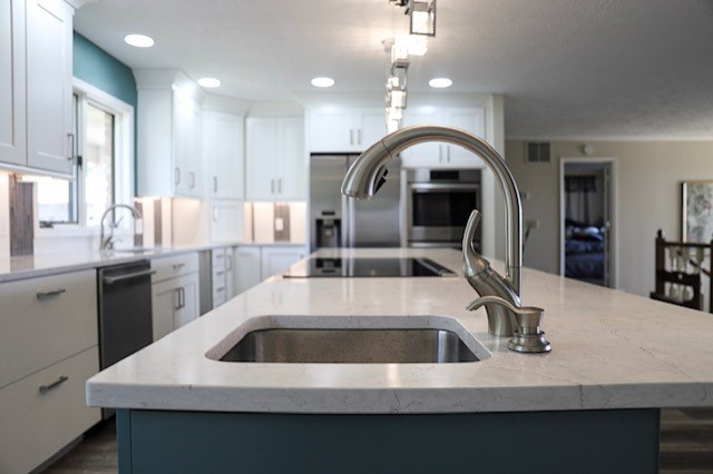 Kitchen pantry - large modern l-shaped vinyl floor and gray floor kitchen pantry idea with an undermount sink, recessed-panel cabinets, white cabinets, quartz countertops, white backsplash, glass tile backsplash, stainless steel appliances, an island and white countertops
