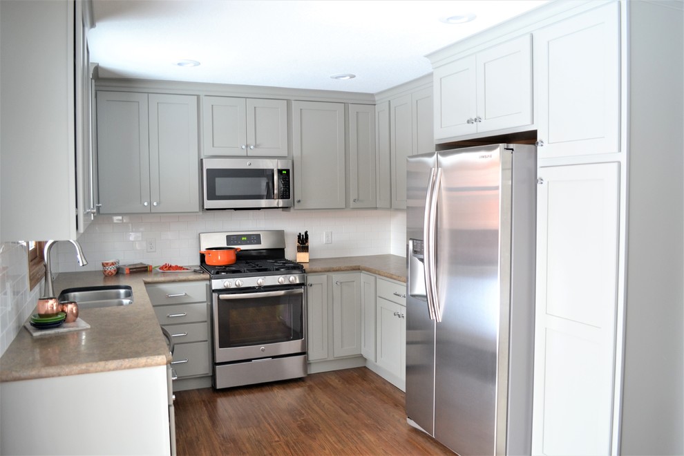 Mid-sized transitional u-shaped vinyl floor and brown floor enclosed kitchen photo with an undermount sink, flat-panel cabinets, gray cabinets, laminate countertops, white backsplash, subway tile backsplash, stainless steel appliances and no island
