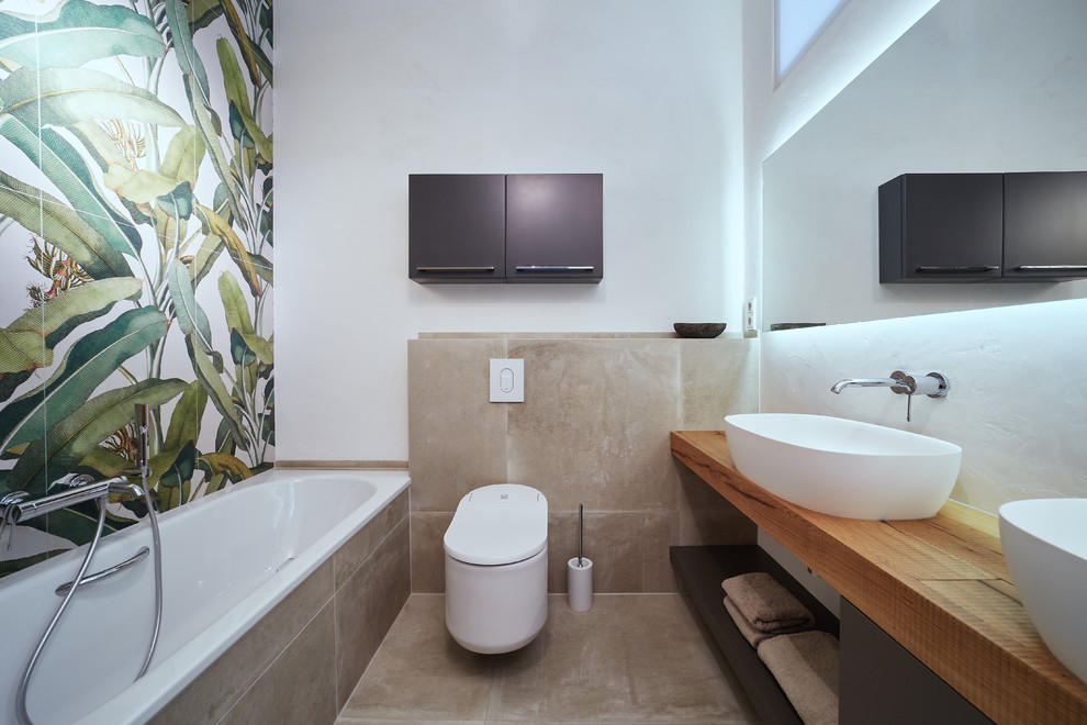 This is an example of a mid-sized contemporary bathroom in Other with open cabinets, grey cabinets, a drop-in tub, a two-piece toilet, white tile, stone tile, white walls, brick floors, a vessel sink, wood benchtops, brown floor and brown benchtops.