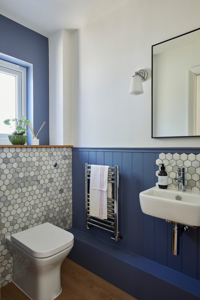 This is an example of a small transitional powder room in London with a one-piece toilet, gray tile, marble, blue walls, vinyl floors, a wall-mount sink, wood benchtops, beige floor, brown benchtops and panelled walls.