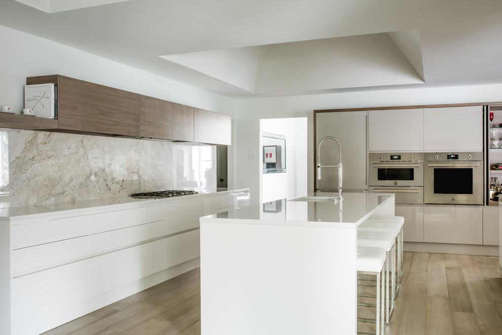 This is an example of a mid-sized modern l-shaped kitchen in Dallas with an undermount sink, flat-panel cabinets, white cabinets, quartz benchtops, white splashback, stone slab splashback, stainless steel appliances, medium hardwood floors, with island and brown floor.