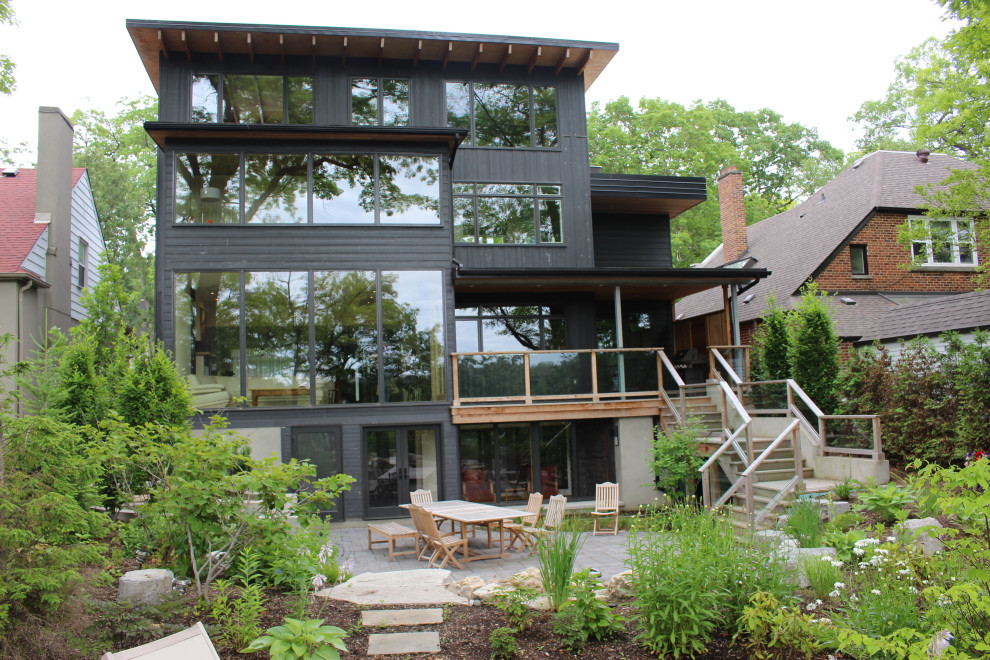 Large midcentury three-storey grey house exterior in Toronto with stone veneer, a flat roof and a green roof.
