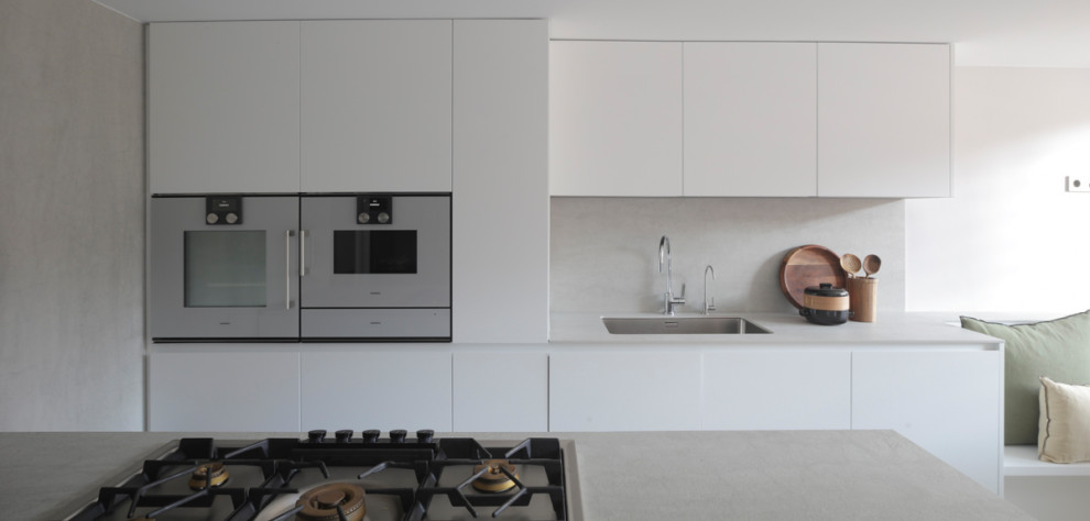 Design ideas for a mid-sized u-shaped eat-in kitchen with an integrated sink, glass-front cabinets, grey cabinets, quartz benchtops, grey splashback, engineered quartz splashback, panelled appliances, concrete floors, a peninsula, grey floor, grey benchtop and recessed.