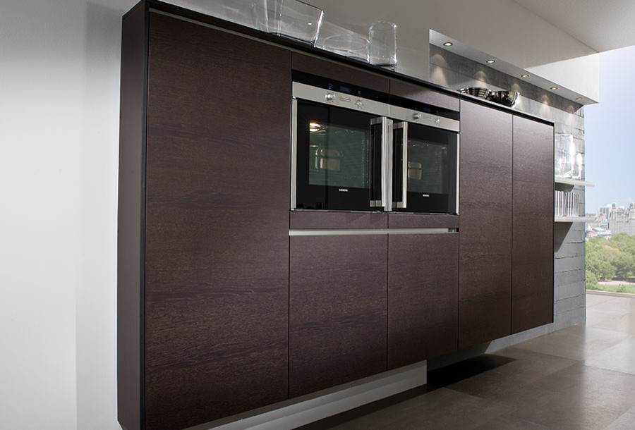 Photo of a contemporary eat-in kitchen in London with an integrated sink, flat-panel cabinets, dark wood cabinets, stainless steel benchtops and with island.