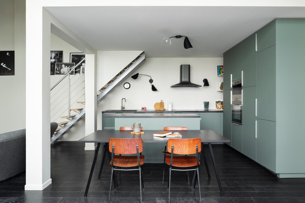 Idée de décoration pour une cuisine ouverte design en L avec un placard à porte plane, des portes de placards vertess, parquet foncé, îlot, un sol noir et plan de travail noir.