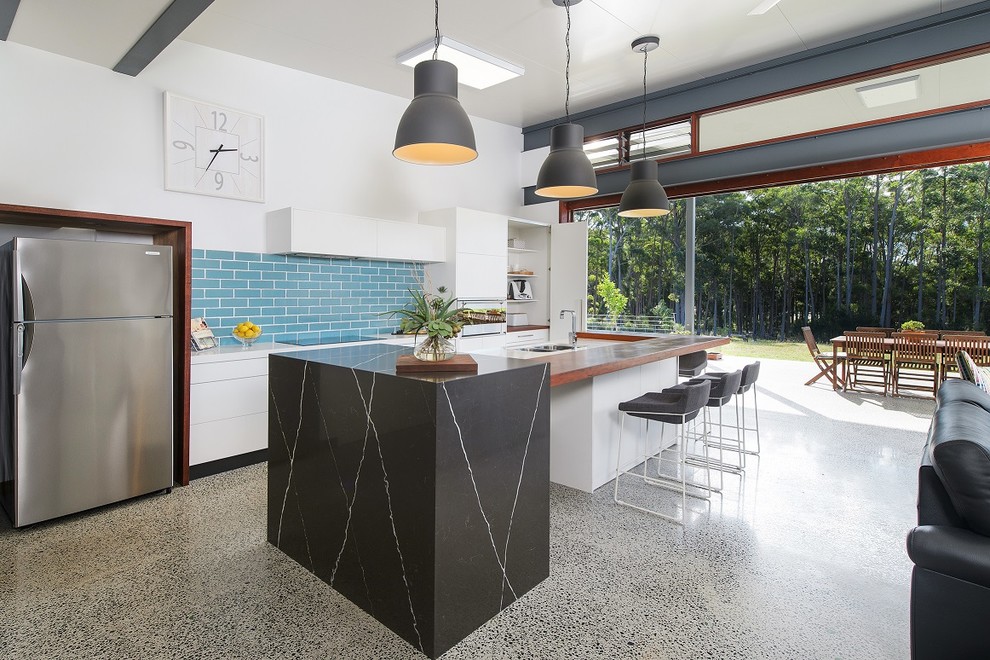 Contemporary galley kitchen with flat-panel cabinets, white cabinets, blue splashback, subway tile splashback, stainless steel appliances and with island.
