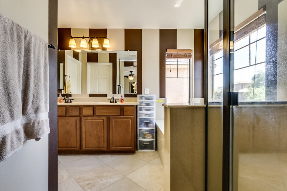 This is an example of a large traditional master bathroom in Phoenix with raised-panel cabinets, medium wood cabinets, a drop-in tub, an alcove shower, a one-piece toilet, brown walls, travertine floors, an integrated sink and marble benchtops.