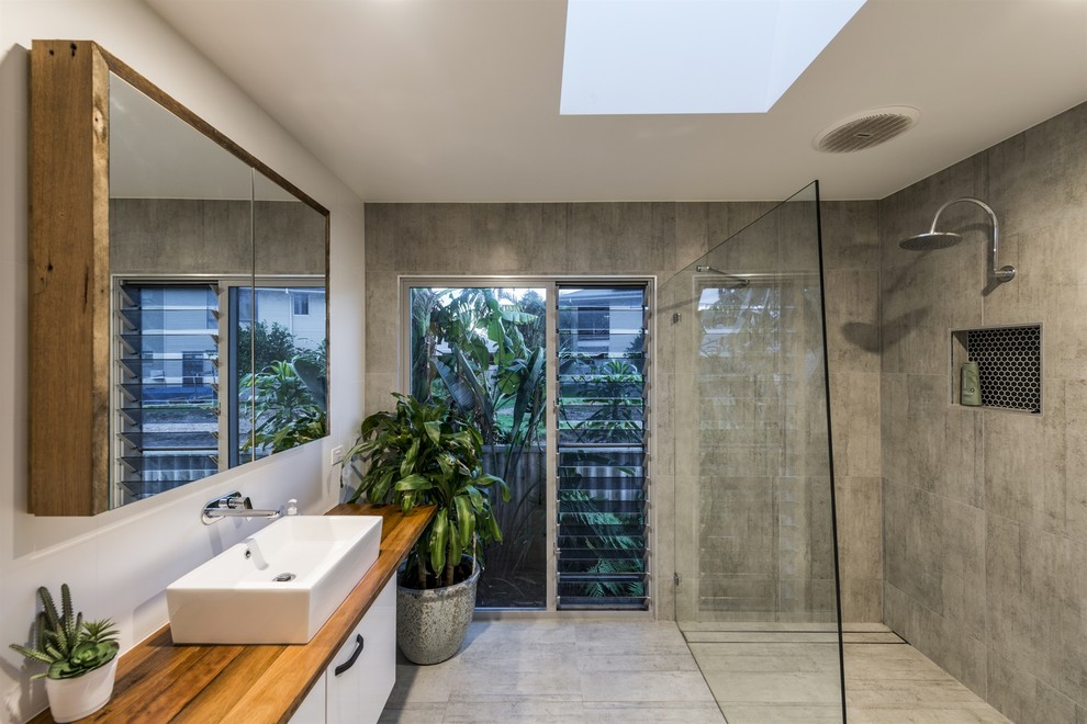 This is an example of a mid-sized contemporary kids bathroom in Gold Coast - Tweed with white cabinets, gray tile, a vessel sink, wood benchtops, an open shower, an open shower, a one-piece toilet, ceramic tile, grey walls, ceramic floors, grey floor, brown benchtops and flat-panel cabinets.