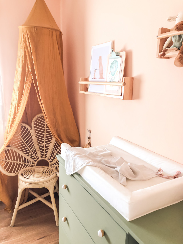 This is an example of a small scandi gender neutral toddler’s room in Barcelona with pink walls and dark hardwood flooring.