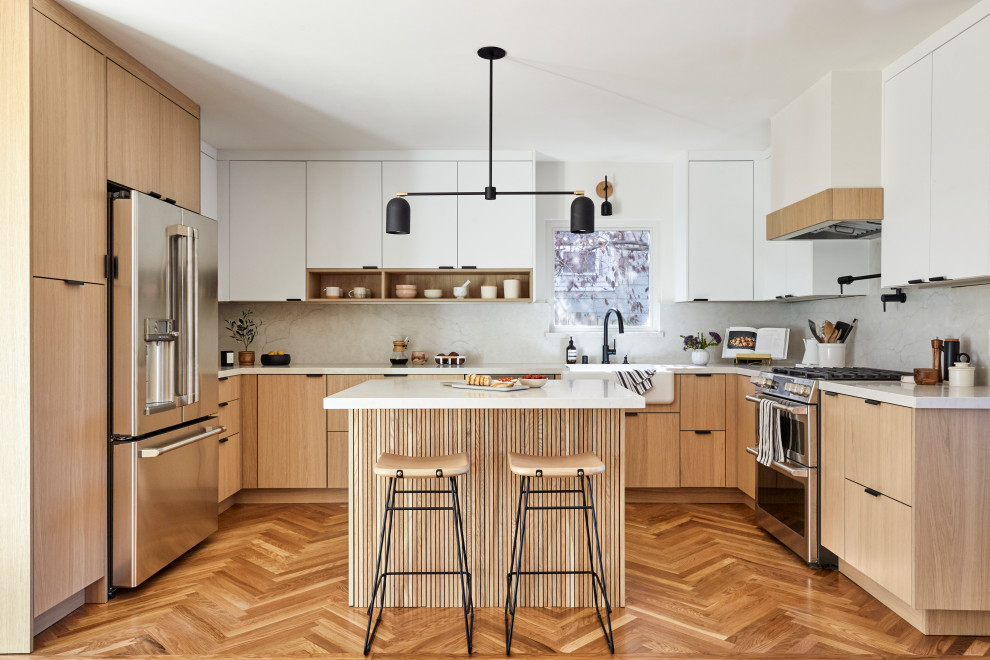 Inspiration for a large scandi u-shaped kitchen/diner in San Francisco with a belfast sink, flat-panel cabinets, light wood cabinets, engineered stone countertops, white splashback, engineered quartz splashback, stainless steel appliances, light hardwood flooring, an island, brown floors and white worktops.
