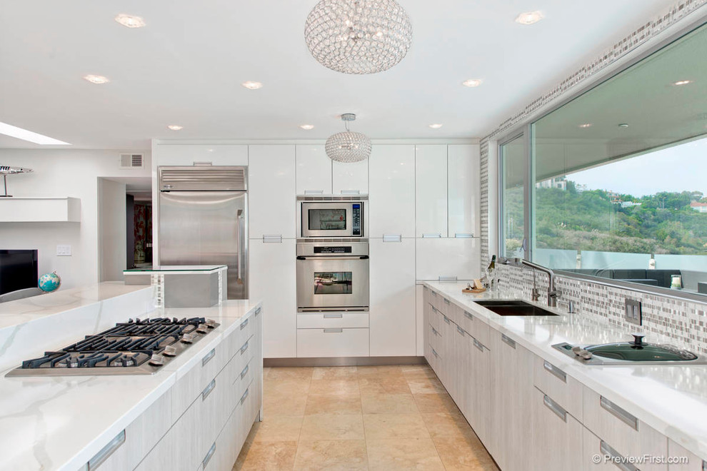 Photo of a mid-sized contemporary l-shaped open plan kitchen in San Diego with an undermount sink, flat-panel cabinets, grey cabinets, stainless steel appliances, a peninsula, travertine floors, multi-coloured splashback, mosaic tile splashback, solid surface benchtops, beige floor and white benchtop.