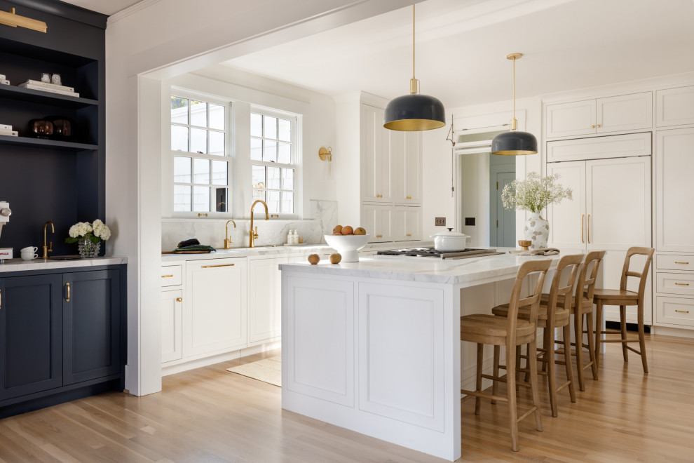 Inspiration for a transitional l-shaped medium tone wood floor and brown floor kitchen remodel in Seattle with recessed-panel cabinets, white cabinets, white backsplash, stone slab backsplash, paneled appliances, an island and white countertops