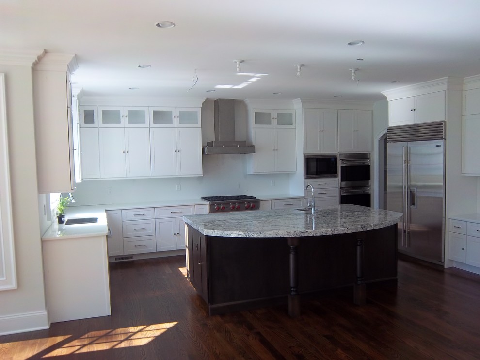 Inspiration for a large transitional u-shaped dark wood floor and brown floor eat-in kitchen remodel with shaker cabinets, white cabinets, white backsplash, stainless steel appliances, an island, an undermount sink, solid surface countertops and white countertops