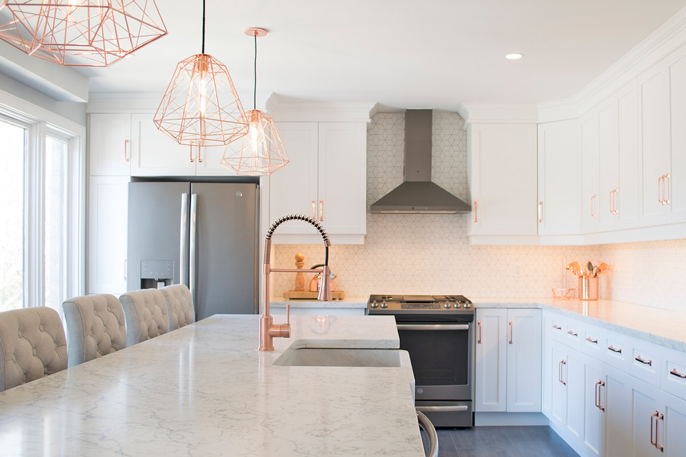 Transitional gray floor open concept kitchen photo with a farmhouse sink, recessed-panel cabinets, white cabinets, quartz countertops, white backsplash, mosaic tile backsplash, stainless steel appliances, an island and white countertops