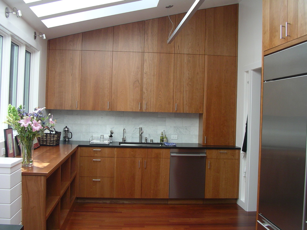 This is an example of a contemporary kitchen in San Francisco with stainless steel appliances, an undermount sink, flat-panel cabinets, medium wood cabinets, white splashback, stone tile splashback and wood benchtops.