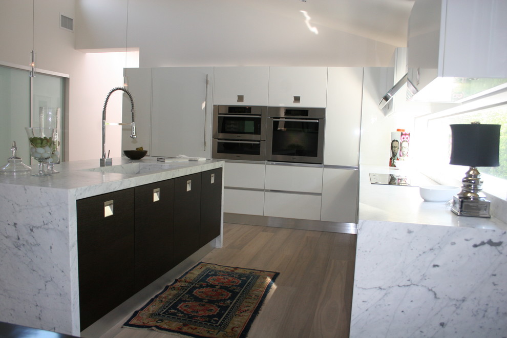 Photo of a modern kitchen in Los Angeles with marble benchtops, an integrated sink, flat-panel cabinets and stainless steel appliances.