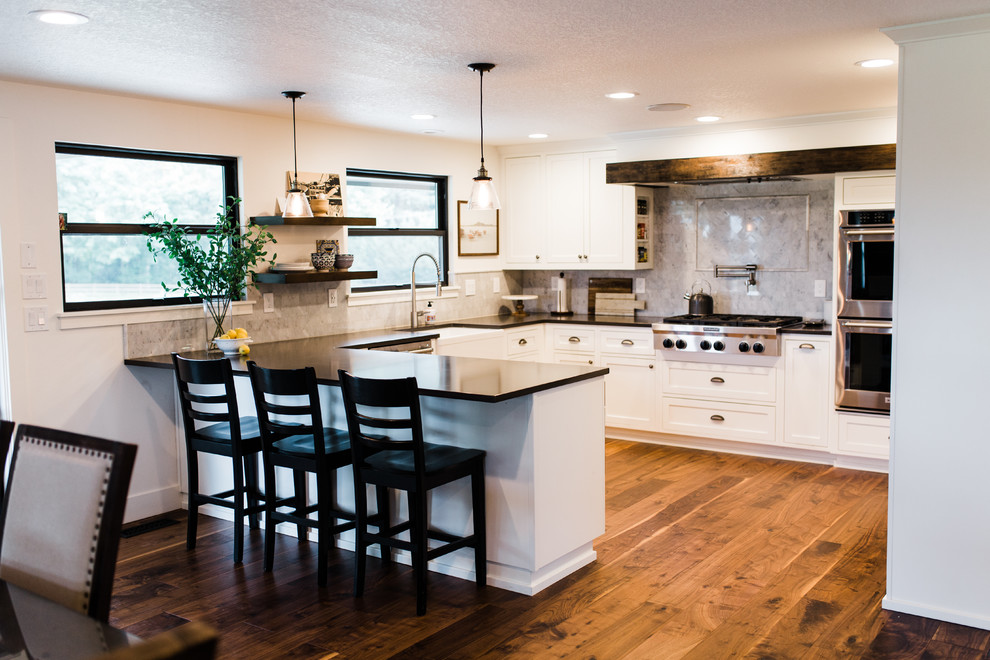 Inspiration for a large transitional u-shaped medium tone wood floor and brown floor eat-in kitchen remodel in Phoenix with a farmhouse sink, shaker cabinets, white cabinets, quartzite countertops, gray backsplash, marble backsplash, stainless steel appliances and a peninsula