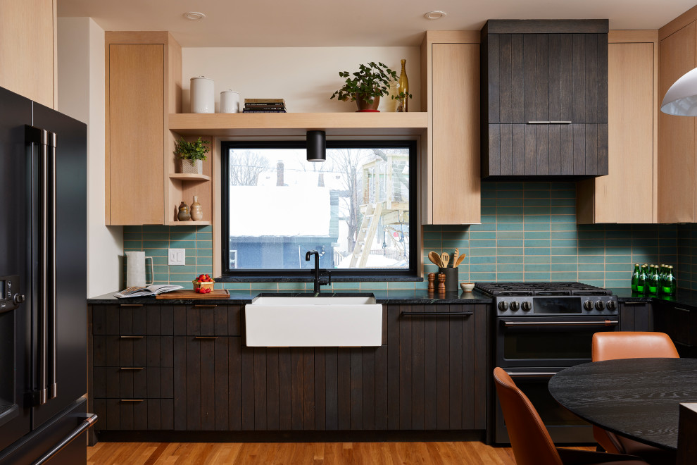 Moderne Wohnküche ohne Insel in U-Form mit Landhausspüle, flächenbündigen Schrankfronten, dunklen Holzschränken, Küchenrückwand in Blau, schwarzen Elektrogeräten, braunem Holzboden, braunem Boden und schwarzer Arbeitsplatte in Minneapolis