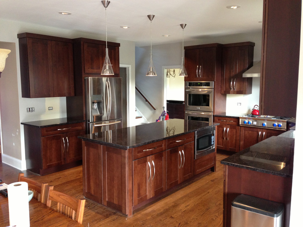 Large transitional u-shaped medium tone wood floor eat-in kitchen photo in Chicago with a farmhouse sink, shaker cabinets, medium tone wood cabinets, granite countertops, stainless steel appliances and an island