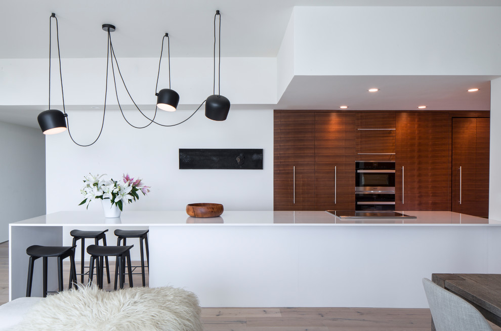 Inspiration for a modern galley eat-in kitchen in Los Angeles with flat-panel cabinets, medium wood cabinets, panelled appliances, light hardwood floors, a peninsula, beige floor and white benchtop.