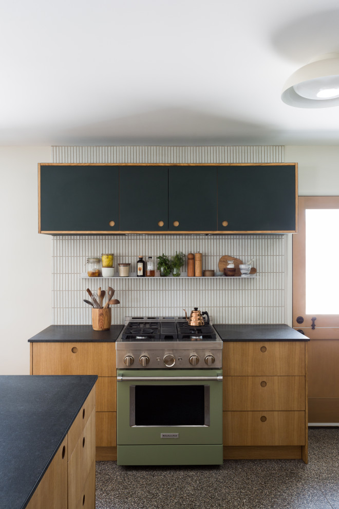 Inredning av ett 50 tals litet svart svart l-kök, med en undermonterad diskho, släta luckor, gröna skåp, granitbänkskiva, vitt stänkskydd, stänkskydd i keramik, terrazzogolv, en köksö och flerfärgat golv