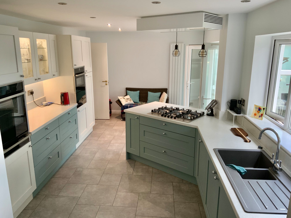 This is an example of a large country eat-in kitchen in Buckinghamshire with shaker cabinets, green cabinets, laminate benchtops, vinyl floors, a peninsula and white benchtop.