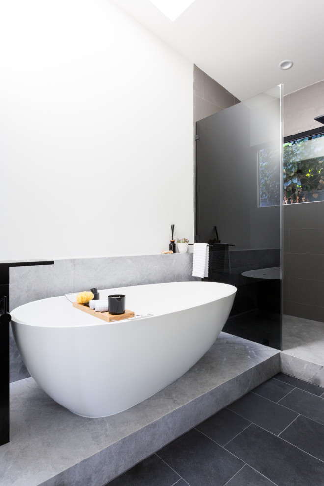 Photo of a mid-sized modern master wet room bathroom in Los Angeles with flat-panel cabinets, black cabinets, a freestanding tub, a one-piece toilet, white tile, white walls, slate floors, an undermount sink, marble benchtops, grey floor, a hinged shower door, grey benchtops, a shower seat, a double vanity, a built-in vanity and vaulted.