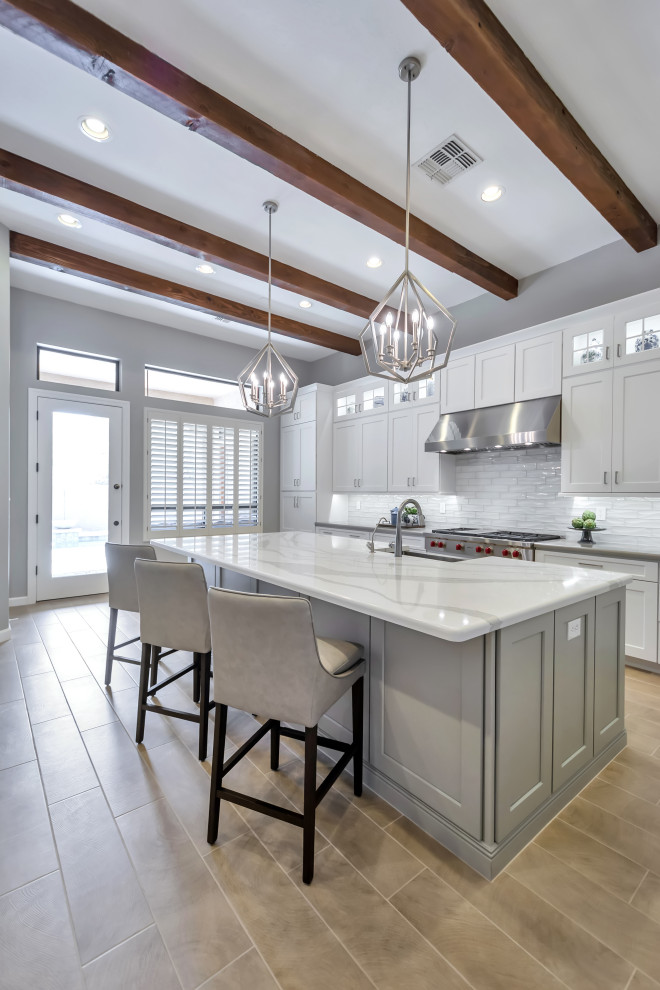 Example of a large transitional l-shaped porcelain tile and brown floor eat-in kitchen design in Phoenix with a farmhouse sink, shaker cabinets, white cabinets, quartz countertops, white backsplash, subway tile backsplash, stainless steel appliances, an island and gray countertops