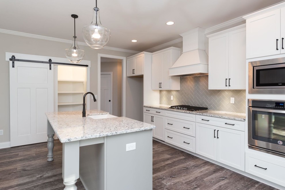 This is an example of a mid-sized transitional single-wall open plan kitchen in Raleigh with a farmhouse sink, shaker cabinets, white cabinets, granite benchtops, grey splashback, ceramic splashback, stainless steel appliances, vinyl floors, with island and brown floor.