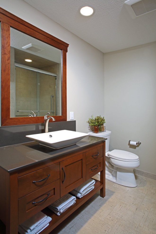 Inredning av ett modernt stort grå grått toalett, med släta luckor, skåp i mellenmörkt trä, en toalettstol med hel cisternkåpa, klinkergolv i porslin, ett fristående handfat, bänkskiva i akrylsten och beiget golv