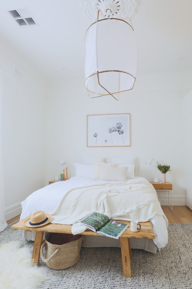 Photo of a mid-sized beach style master bedroom in Sydney with white walls, light hardwood floors and no fireplace.