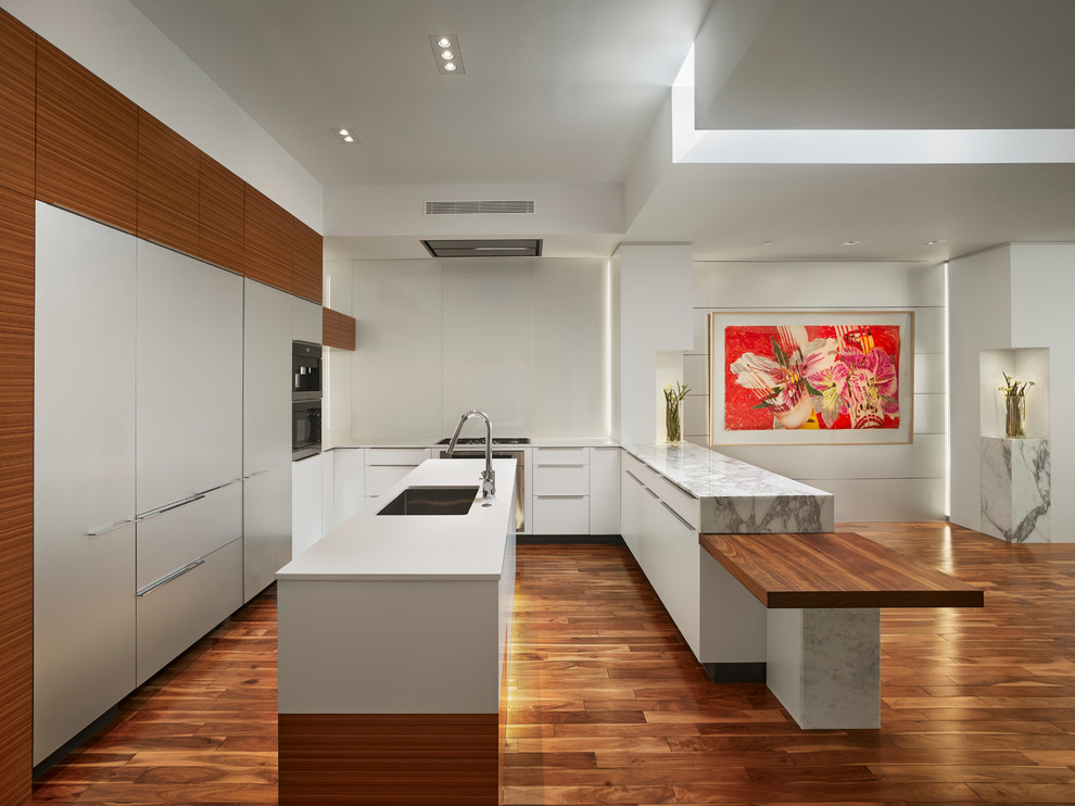 Inspiration for a large contemporary u-shaped open plan kitchen in Philadelphia with a drop-in sink, flat-panel cabinets, white cabinets, marble benchtops, white splashback, stainless steel appliances, medium hardwood floors and multiple islands.