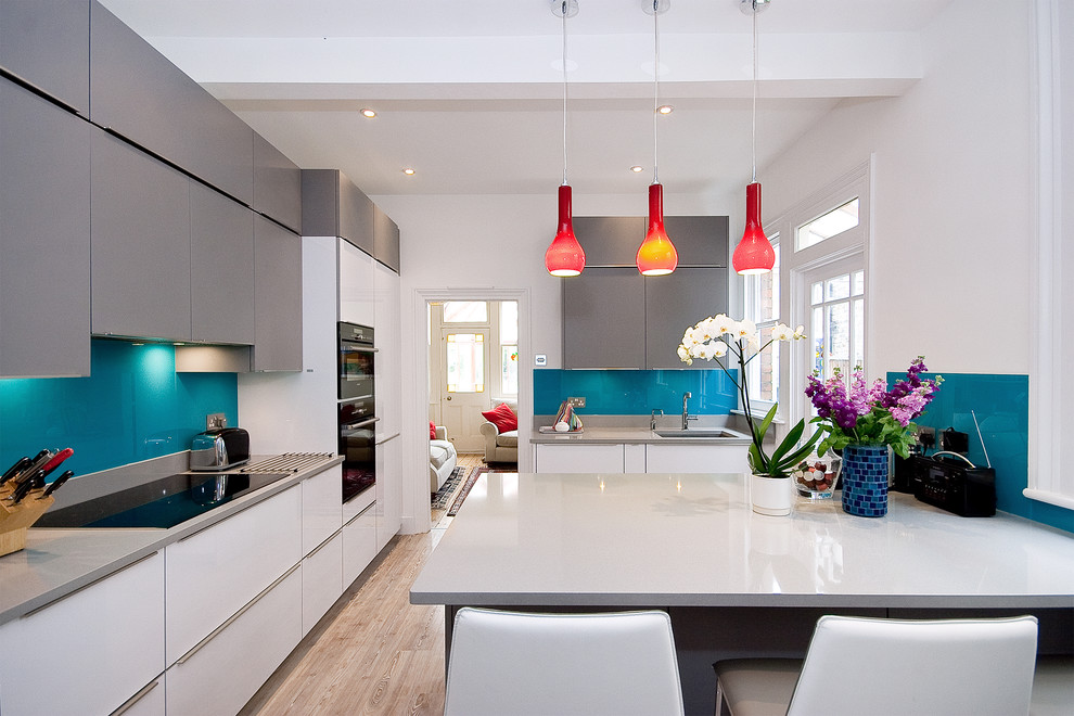 Photo of a contemporary kitchen in London with an undermount sink, flat-panel cabinets, white cabinets, blue splashback, glass sheet splashback, light hardwood floors and a peninsula.