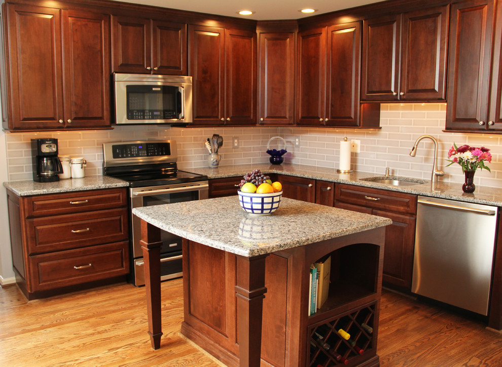 Mid-sized transitional l-shaped medium tone wood floor eat-in kitchen photo in DC Metro with an undermount sink, raised-panel cabinets, medium tone wood cabinets, granite countertops, gray backsplash, glass tile backsplash, stainless steel appliances and an island