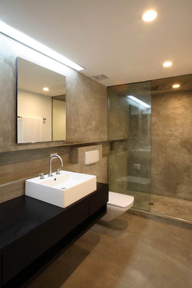 Photo of a large contemporary master bathroom in New York with a vessel sink, wood benchtops, a wall-mount toilet, concrete floors, black benchtops, an open shower, beige tile, black walls, beige floor and an open shower.