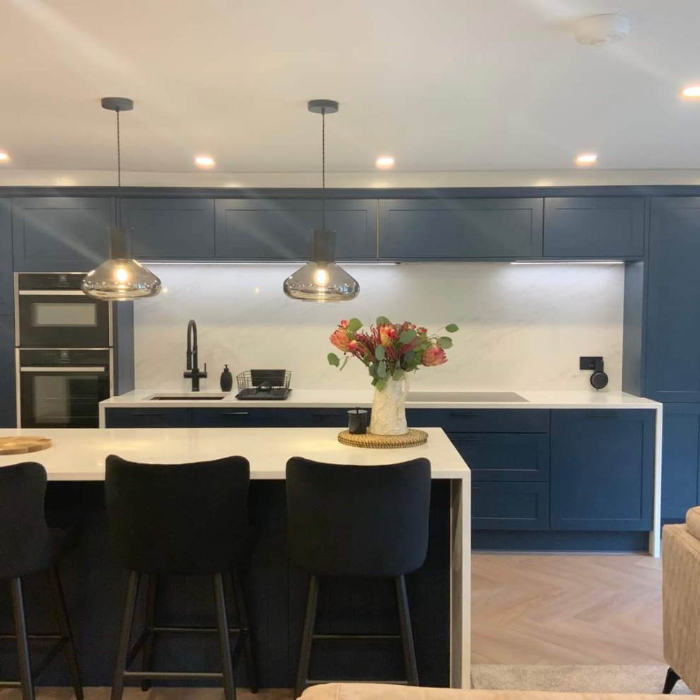 Bild på ett stort funkis vit vitt kök och matrum, med skåp i shakerstil, blå skåp, bänkskiva i kvartsit, vitt stänkskydd, integrerade vitvaror, vinylgolv, en köksö och brunt golv