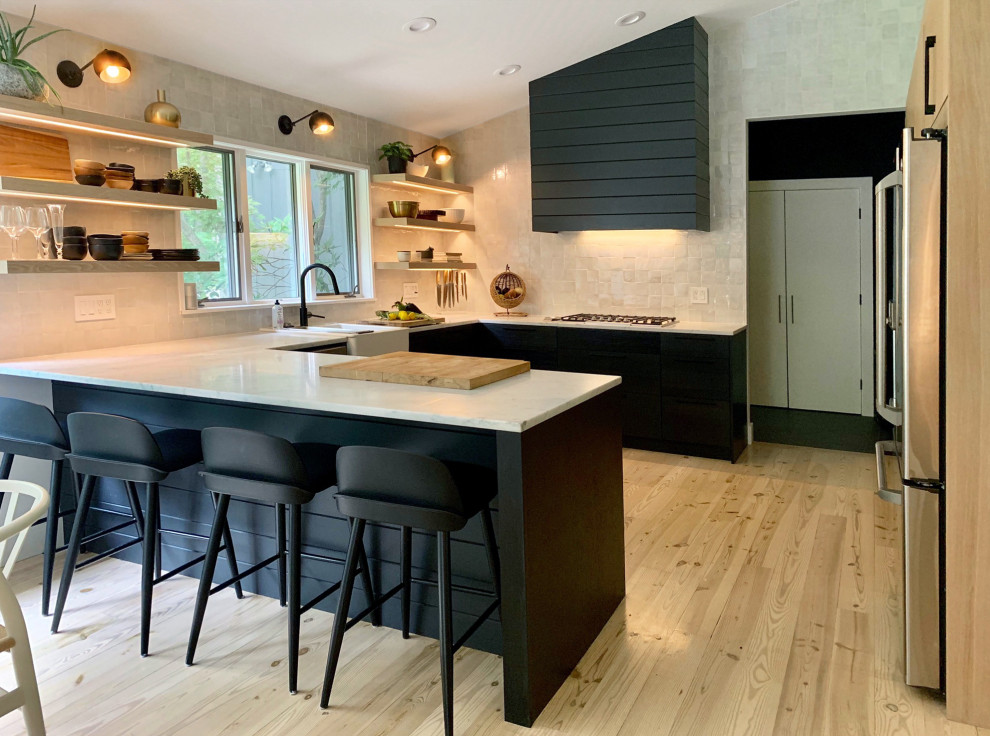 This is an example of a large modern u-shaped eat-in kitchen in New York with a farmhouse sink, flat-panel cabinets, black cabinets, marble benchtops, white splashback, terra-cotta splashback, stainless steel appliances, light hardwood floors, beige floor and white benchtop.