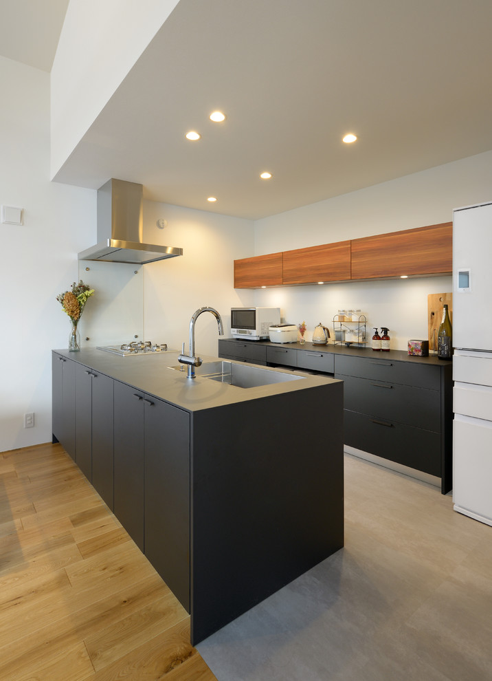Photo of a scandinavian kitchen in Other with a single-bowl sink, flat-panel cabinets, black cabinets, stainless steel benchtops, concrete floors, a peninsula, grey floor and black benchtop.