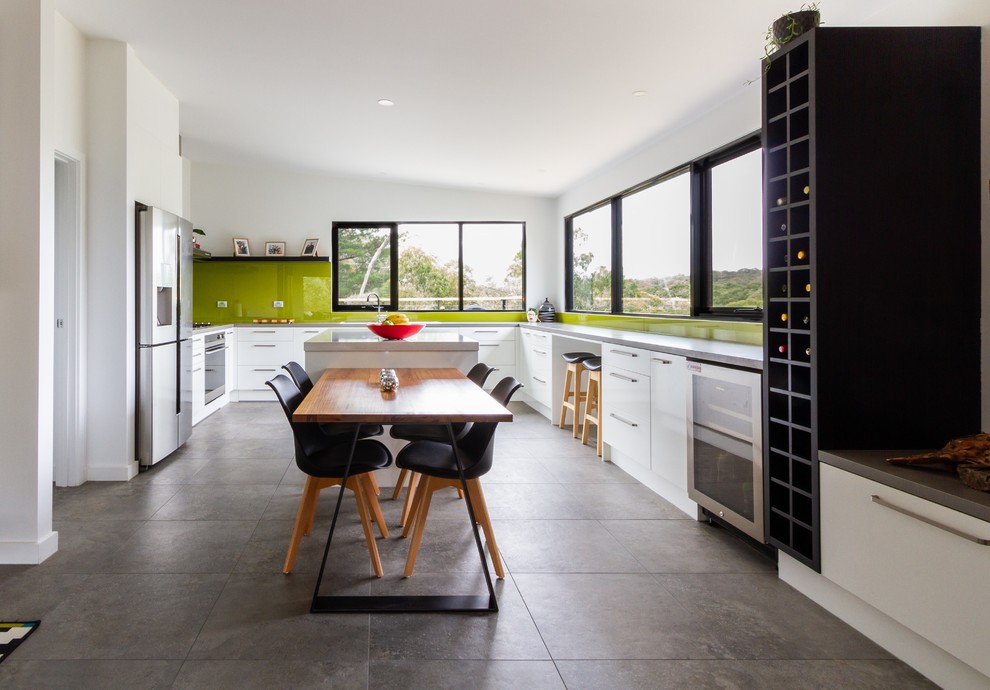 Photo of a large contemporary u-shaped eat-in kitchen in Melbourne with flat-panel cabinets, white cabinets, quartz benchtops, green splashback, glass sheet splashback, stainless steel appliances, porcelain floors, with island, grey floor and grey benchtop.