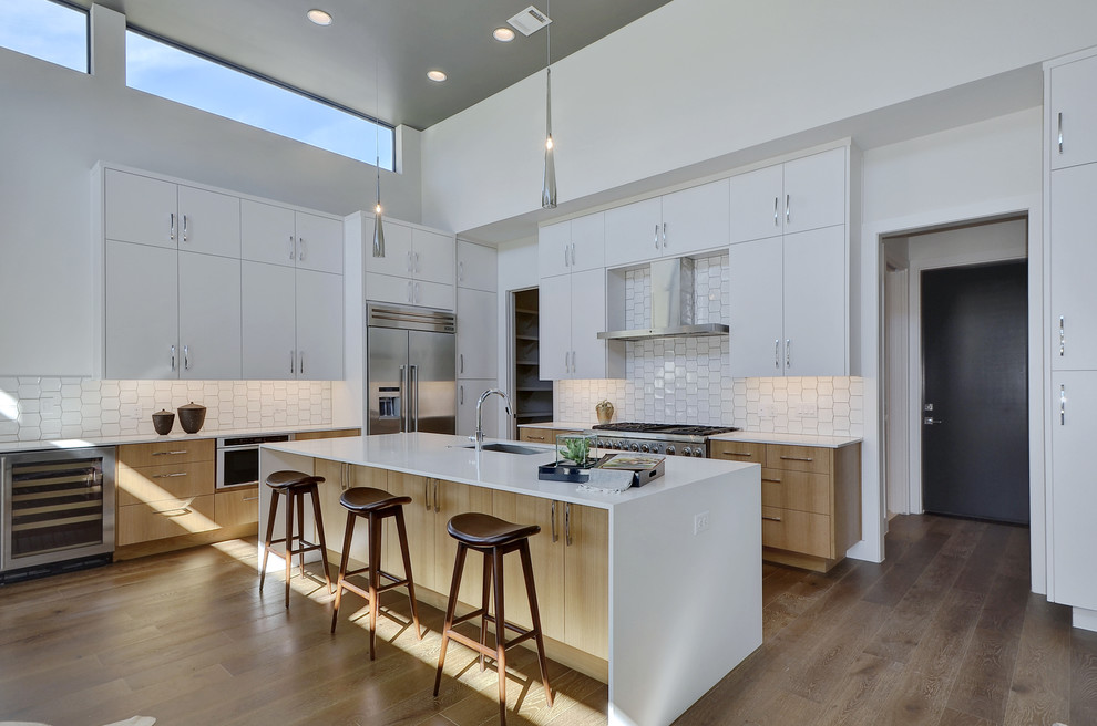 Contemporary u-shaped eat-in kitchen in Austin with an undermount sink, flat-panel cabinets, light wood cabinets, white splashback, stainless steel appliances, medium hardwood floors, with island and brown floor.