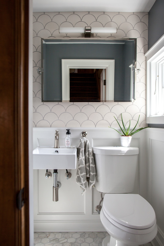 Design ideas for a small transitional powder room in Minneapolis with a two-piece toilet, white tile, ceramic tile, grey walls, marble floors, a wall-mount sink, white cabinets and grey floor.