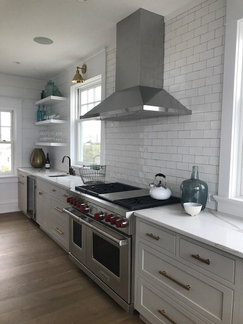 This is an example of a large country l-shaped eat-in kitchen in Philadelphia with a farmhouse sink, beaded inset cabinets, grey cabinets, quartzite benchtops, white splashback, ceramic splashback, stainless steel appliances, medium hardwood floors, with island and orange floor.