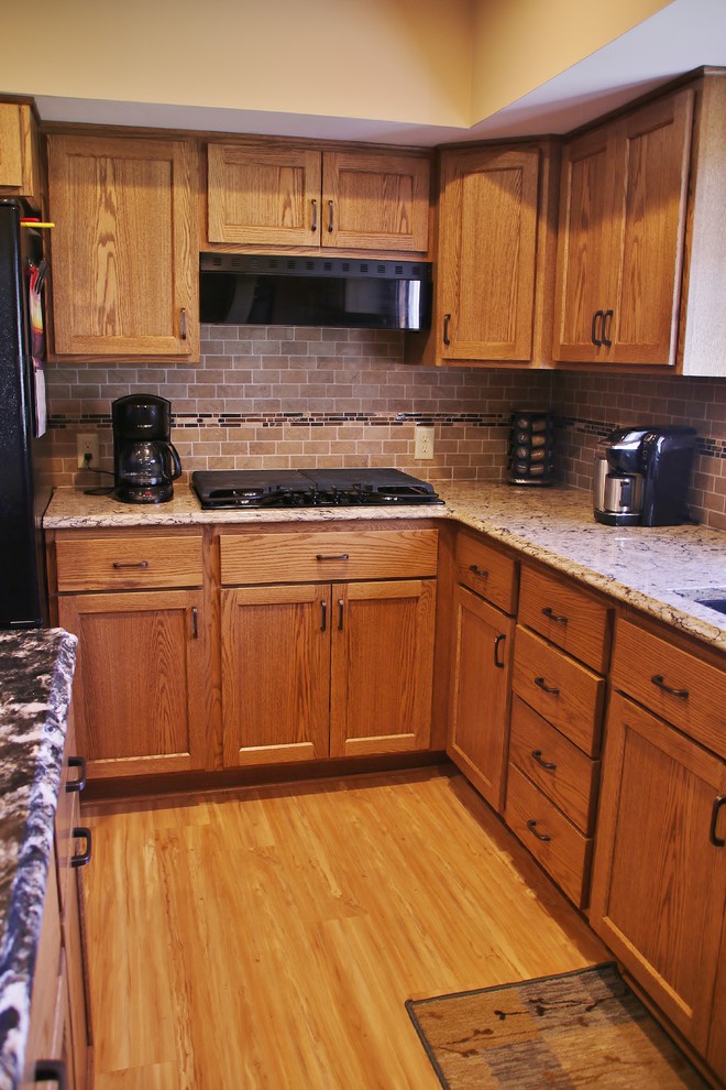 Inspiration for a mid-sized l-shaped eat-in kitchen remodel with flat-panel cabinets, medium tone wood cabinets, quartz countertops, beige backsplash, black appliances and an island