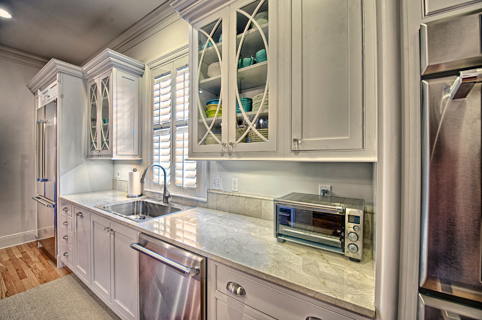 This is an example of a mid-sized transitional eat-in kitchen in New Orleans with beaded inset cabinets, white cabinets, marble benchtops, stainless steel appliances, light hardwood floors, with island, beige splashback and travertine splashback.