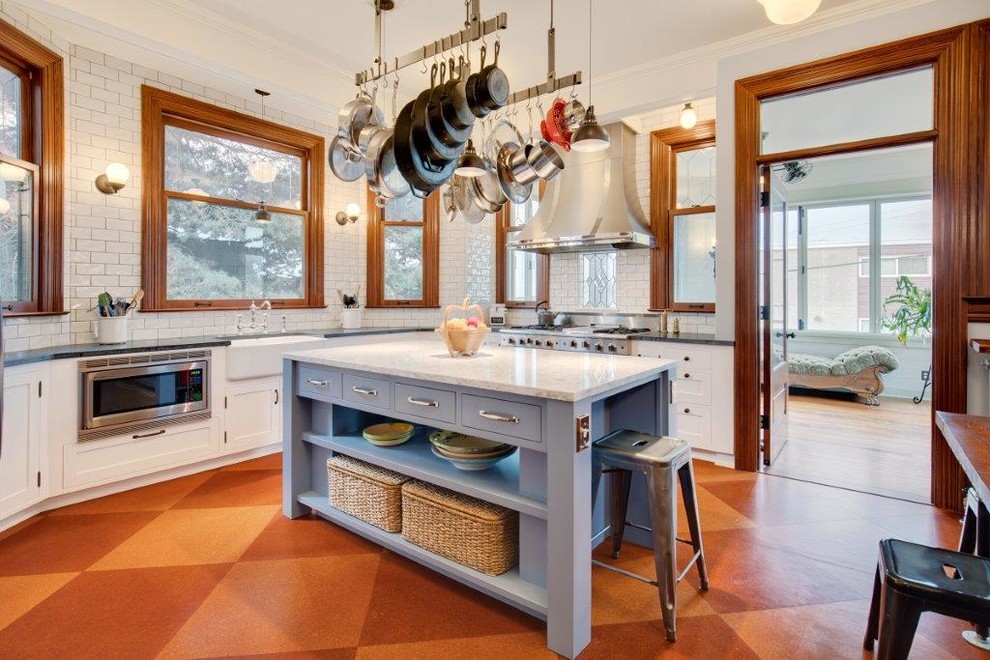 Photo of a mid-sized country u-shaped eat-in kitchen in Seattle with a farmhouse sink, shaker cabinets, white cabinets, quartz benchtops, white splashback, subway tile splashback, white appliances, cork floors, with island and brown floor.